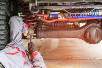 Car mechanic in grey uniform using a wrench to tighten the nut under the car for maintenance, Automotive industry and garage concepts.
