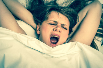 Young woman is yawning in bed after sleeping