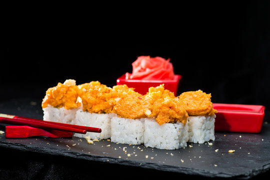 Traditional Japanese cuisine.  Selective focus on sushi rolls and breaded pieces of shrimp on dark background, near ginger and crumbs