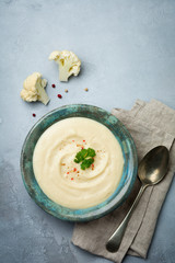 Vegetarian white soup cream from cauliflower in a vintage ceramic plate on a light concrete background. Selective focus. top view. Copy space.