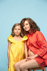 Pregnant mother with teen daughter. Family studio portrait over blue background