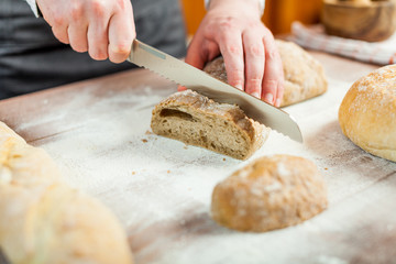 Male hands cutting fresh bread on the wooden table, selective focus