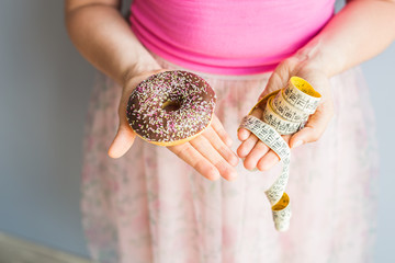 Close-up of woman's hands holding a donut and a measuring tape. The concept of healthy eating. Diet.