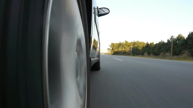 Driving a black sports / super car on a country road. Wheel spinning POV - Point of View, day country side, sunset, fall / winter. Trees on the side. Slow motion speed Right side wheel / driving UK 