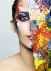 Young female painter with color palette and  acrylic paint on face