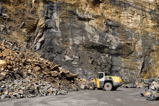 a wheel loader machine working on a large heap of stones in front of a rock face at a quarry