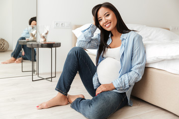 Happy pregnant asian woman leaning on a sofa while sitting