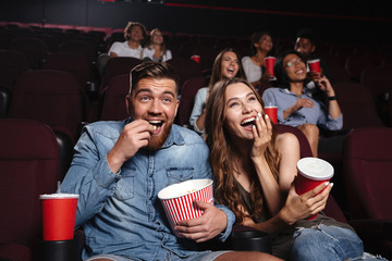 Happy couple eating popcorn and laughing - obrazy, fototapety, plakaty