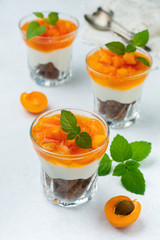 Dessert  Chocolate biscuit, vanilla cream cheese and apricot jam in a glass bowl on a light background. Selective focus.