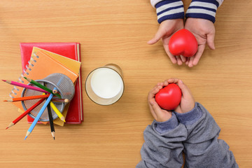 Children's hands holding red heart and notebook with color pencil and milk on wood en table