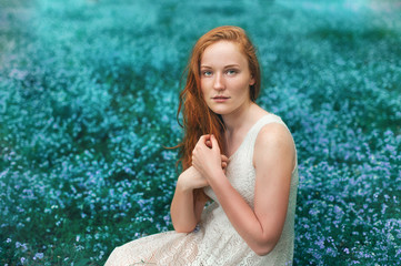 Portrait of beautiful girl sitting on the meadow with blue flowers 