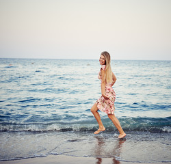 Pretty smiling female running on the beach at sunset. Concept of holidays and travel. 
