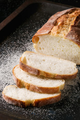 Sliced homemade white wheat bread with wheat flour on old black oven tray as background. Close up