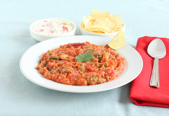 Homemade healthy Indian food pilaf made from brown top millet and lentil in a plate with yogurt salad and potato chips as side dishes.