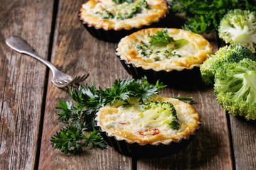 Baked homemade quiche pie in mini metal forms served with fresh greens and fork on old plank wooden background. Close up with space