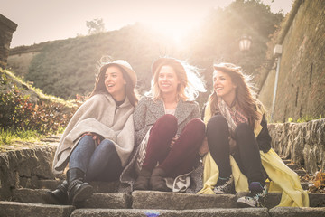 Three young girls sitting on the stairs at the public park and having conversation.