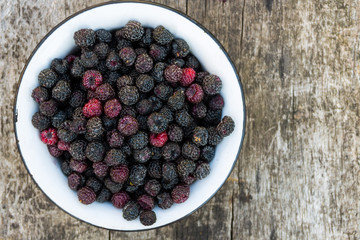 Ripe blackberries in rustic bowl on old wooden background. Top view
