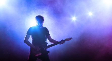 Silhouette of guitar player on stage on blue background with smoke and spotlights	