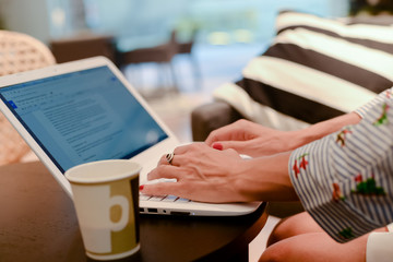 Close up of defocused businesswoman hand busy typing on laptop light background, drinking coffee....