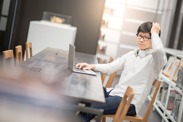 Young Asian man university student feeling frustrated while working with laptop computer in library, self learning and college lifestyle concepts