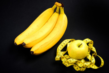 Apple surrounded by yellow tape for measuring near bananas