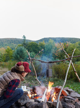 Woman sitting beside camp fire, cooking food, Colgate Lake Wild Forest, Catskill Park, New York State, USA