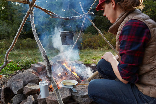 Woman sitting beside camp fire, cooking food, Colgate Lake Wild Forest, Catskill Park, New York State, USA