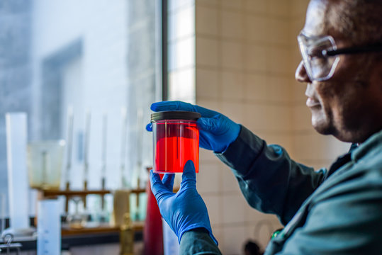 Lab technician looking at beaker of red biofuel in biofuel plant laboratory
