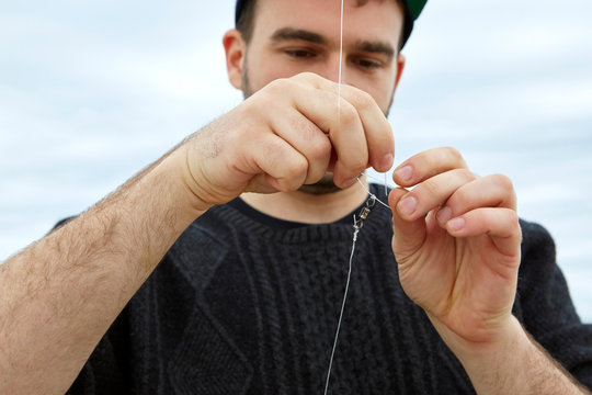 Young man attaching fishing hook to fishing line