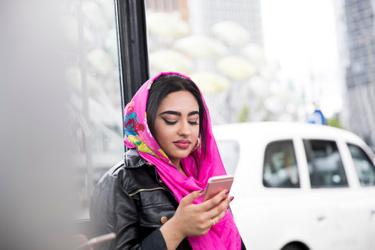 Young woman waiting at bus stop, using smartphone