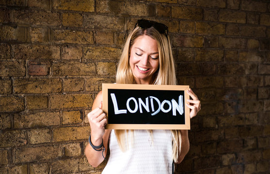 Mid adult standing in front of brick wall, holding sign with 'London' written on it