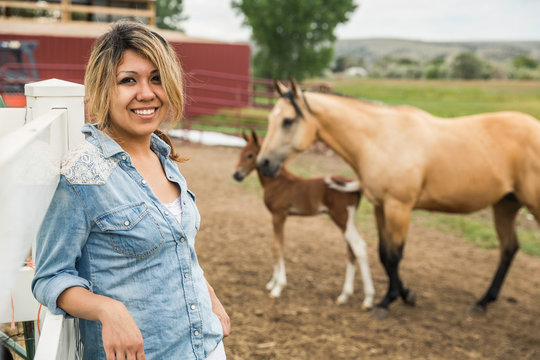 Portrait of young woman on farm, horse and foal in background