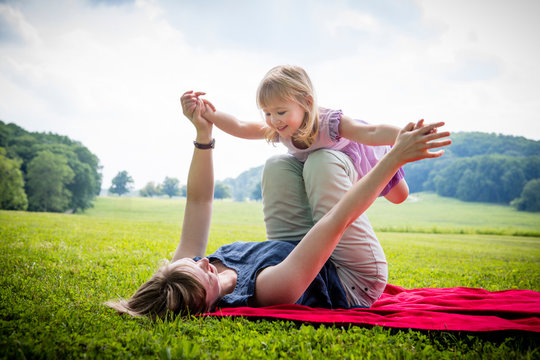 Mid adult woman lying on back balancing daughter in rural field