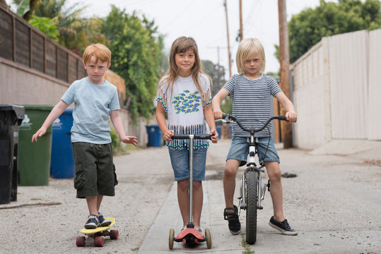Girl and boys in lane with scooter, bicycle and skateboard
