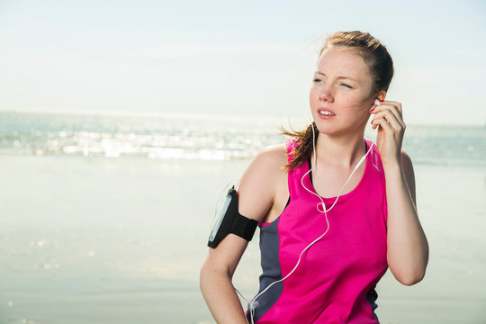 Young woman wearing headphones on beach adjusting music on armband, Folkestone, UK