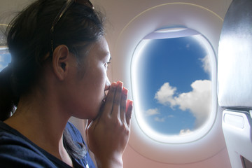 Passengers praying in a flying aircraft while looking out of the window. Portrait of a woman looking out the window of a flying aircraft.