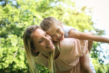 Mother and daughter outdoors in a meadow. Mother carrying her daughter on piggyback.