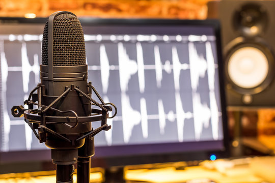 condenser microphone on computer screen showing digital wave & studio monitor speakers background, recording concept