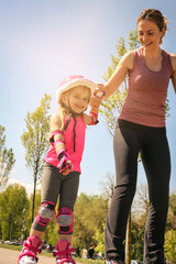 Mother and her little daughter inline skating on sidewalk. Mother and daughter enjoying in spring...