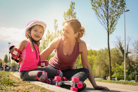 Smiling mother with her little daughter sitting on road after skating.