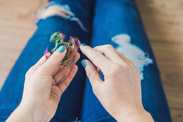 Girl teenager in holey jeans holds in hands and plays with spinner