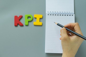 Selective focus on hand holding pencil on white paper note, and colorful wooden alphabet KPI