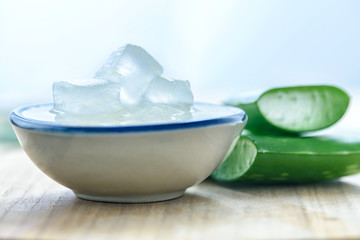 Aloe vera gel on bowl with fresh aloe vera leaves on wooden