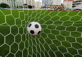 Soccer football in Goal net with green grass field.