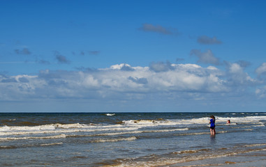 Fototapeta na wymiar Sea beach and two girls entering water