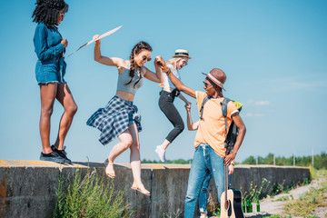 multiethnic group of young friends jumping of parapet together
