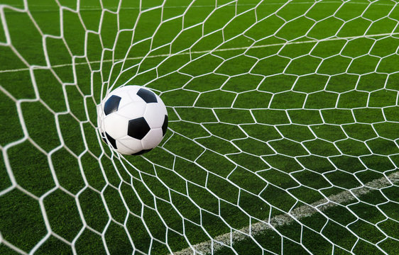 Fototapeta Soccer football in Goal net with green grass field.