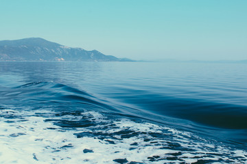Fototapeta na wymiar Sea view of Skiathos island. Waves on the sea left by the ship. Vibrant blue sea and sky.