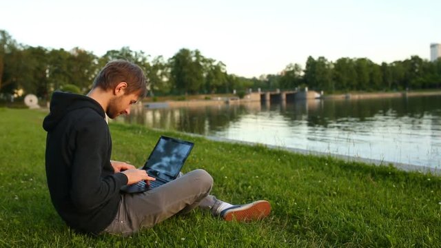 Man freelancer working on the lake with a tablet computer, image at sunset. The lights of a sun.