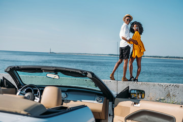 back view of young african american couple standing on parapet at seaside